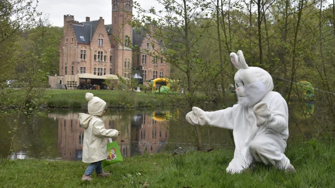 Paashaas in de tuin: Een witte paashaas staat buiten in een groene omgeving bij een stenen gebouw.